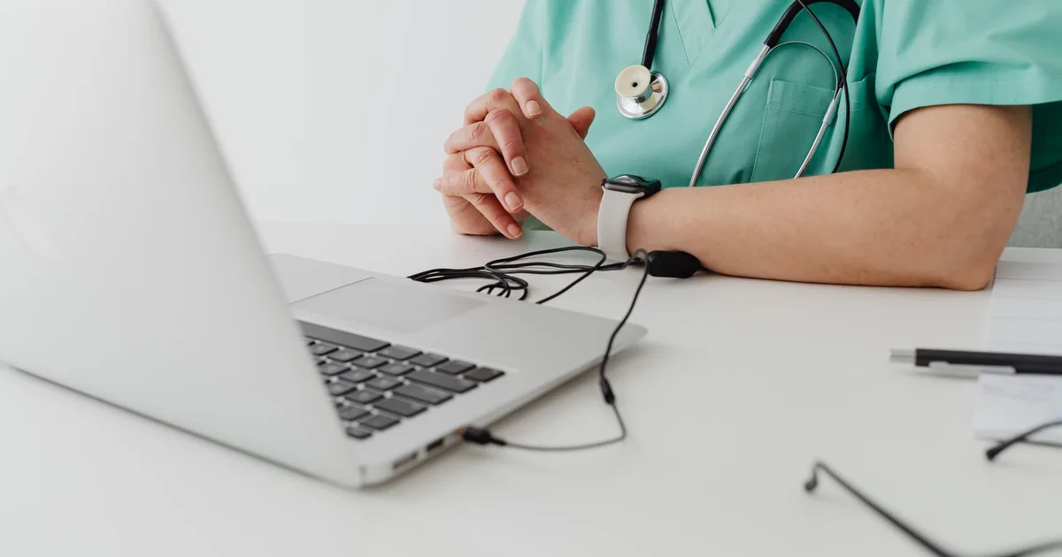 Profesional de salud en uniforme clínico usando un notebook para documentación durante una consulta