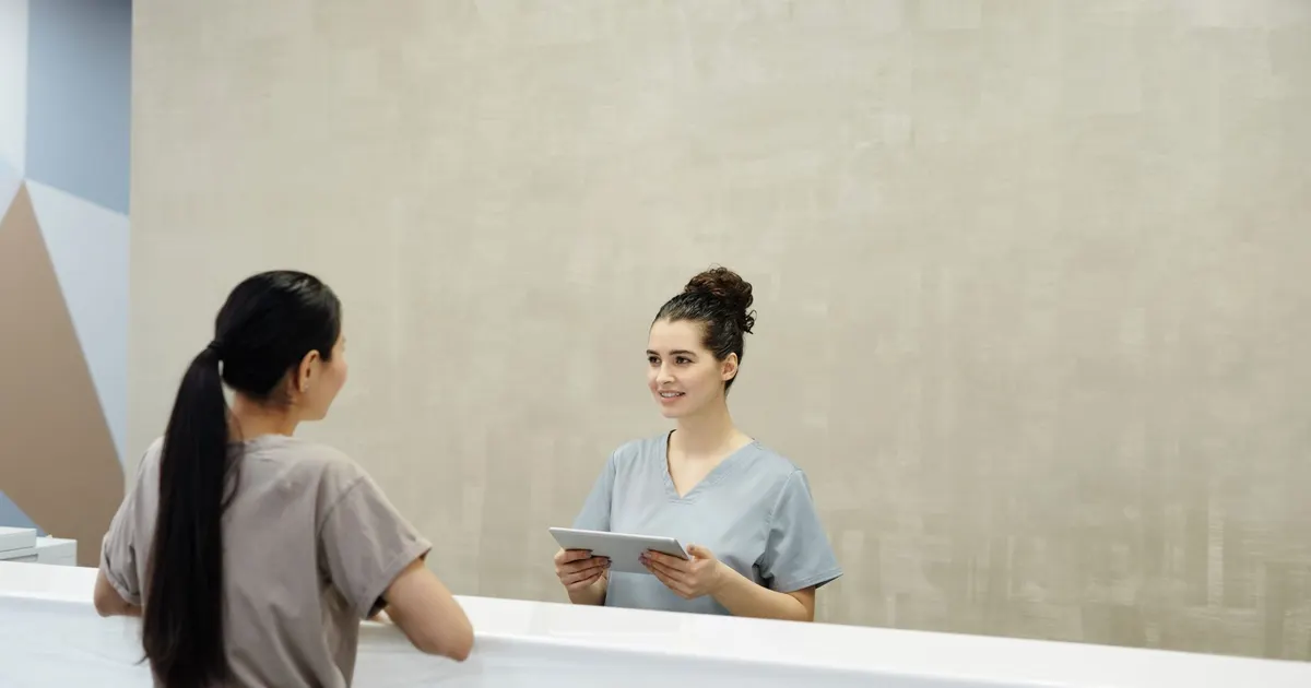 Recepcionista sonriente usa una tablet en el mostrador de recepción de una clínica