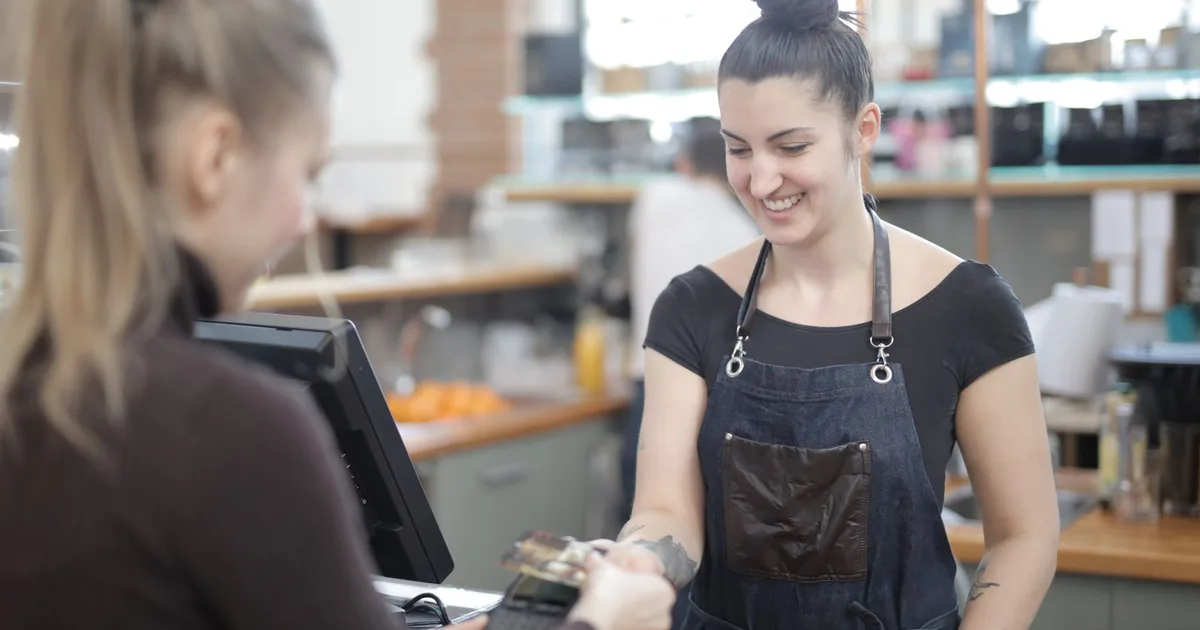 Cajera sonriente ayudando a un cliente a pagar en el mostrador de una tienda