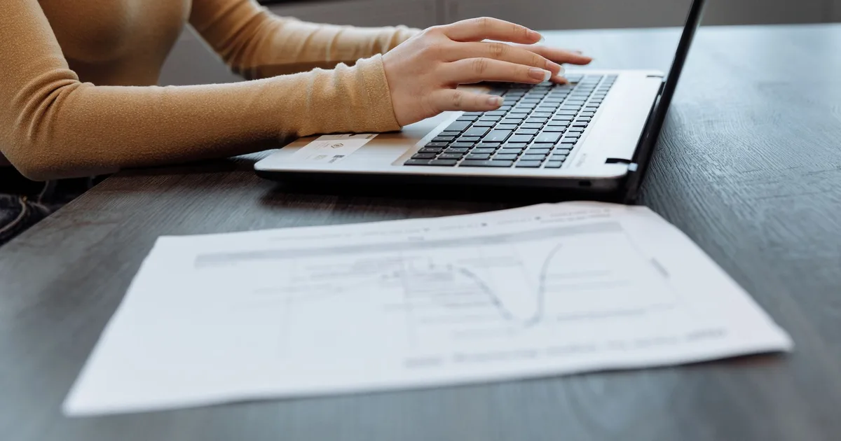 Primer plano de manos escribiendo en un laptop sobre un escritorio con documentos, en una oficina.