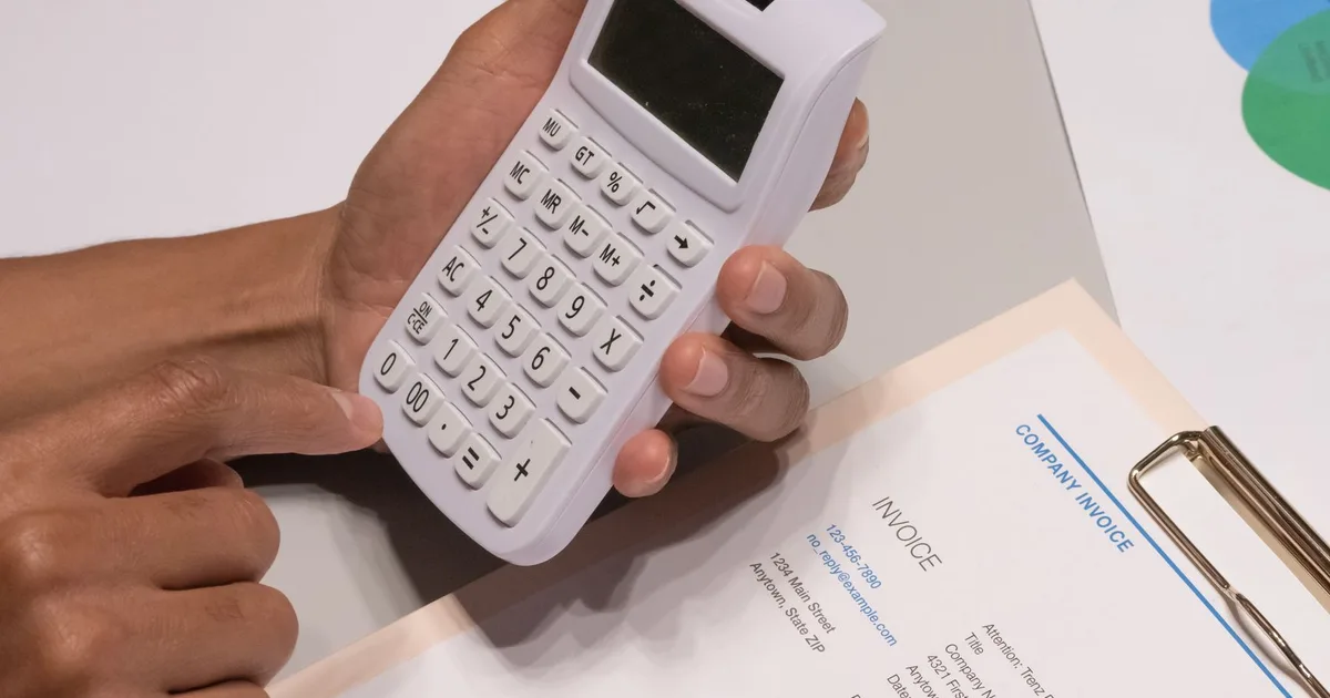 Manos usando una calculadora junto a una factura de empresa sobre un escritorio de oficina