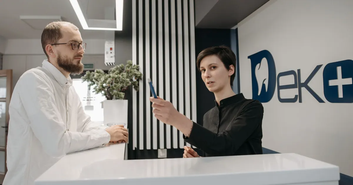 Un hombre conversa con una recepcionista en el mesón de atención de una clínica.