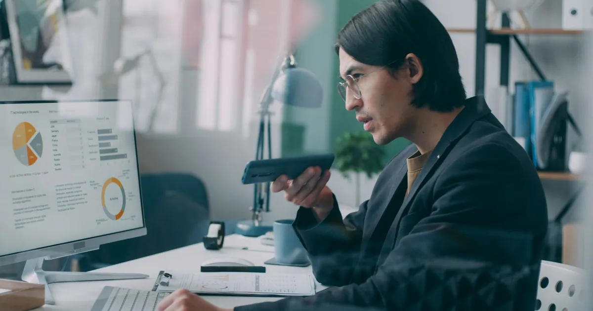 Profesional analiza gráficos de datos en una pantalla de computador mientras habla por teléfono en una oficina
