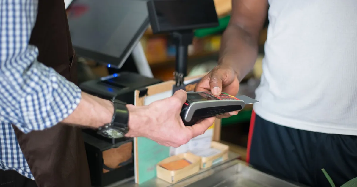 Cliente paga con tarjeta de crédito en el mesón de un local usando un lector de pago