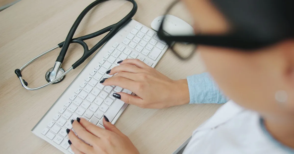 Médico usando el teclado de un computador con un estetoscopio sobre el escritorio