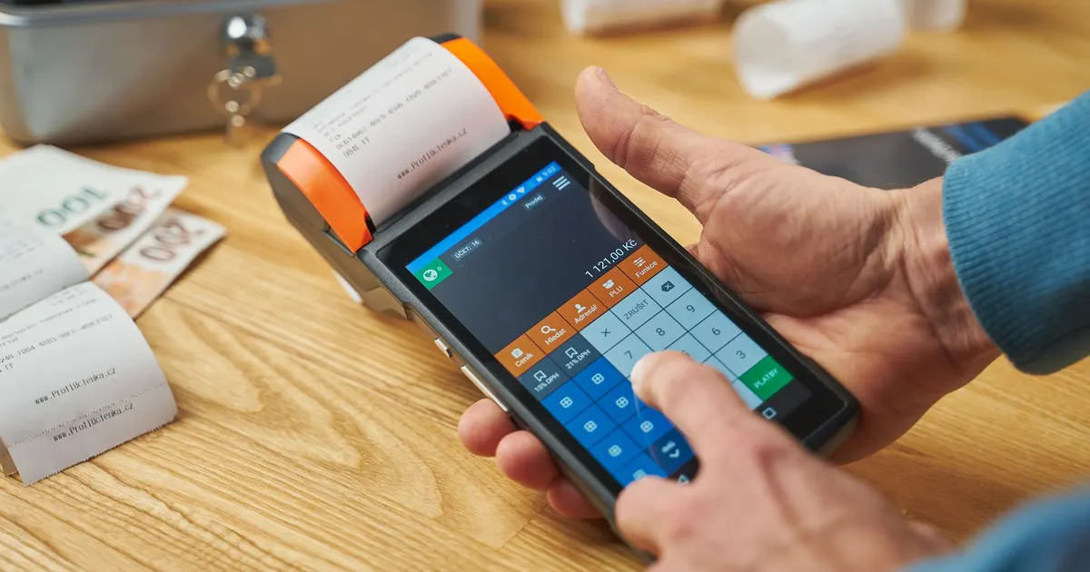 Primer plano de manos operando un terminal de punto de venta con un comprobante impreso
