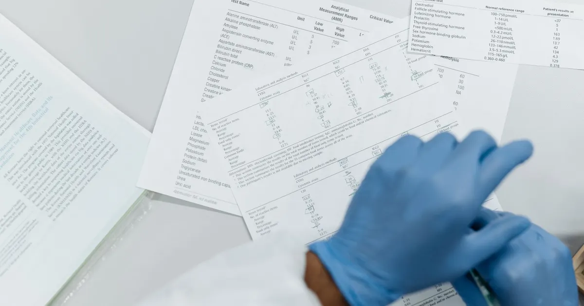 Manos con guantes de látex revisando resultados de exámenes de laboratorio impresos sobre una superficie blanca
