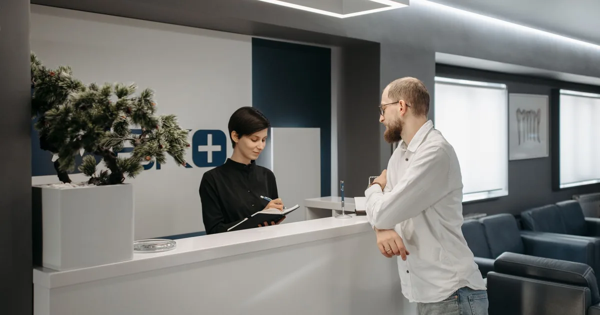 Un hombre conversa con una recepcionista en el mostrador de una clínica moderna