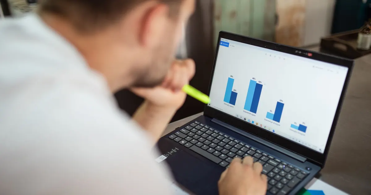 Hombre revisa gráficos de negocio en una laptop desde un ángulo por encima del hombro