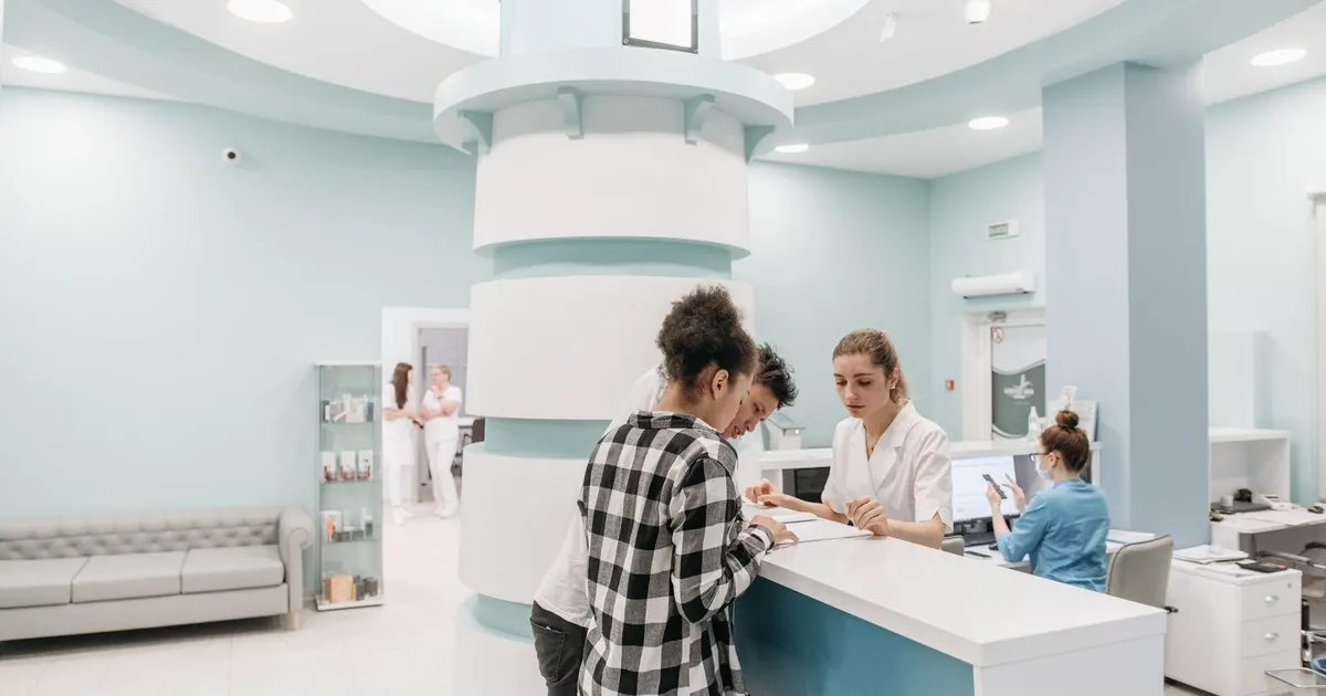 Recepción luminosa y acogedora de una clínica, con personal atendiendo y registrando a los pacientes en el mesón.