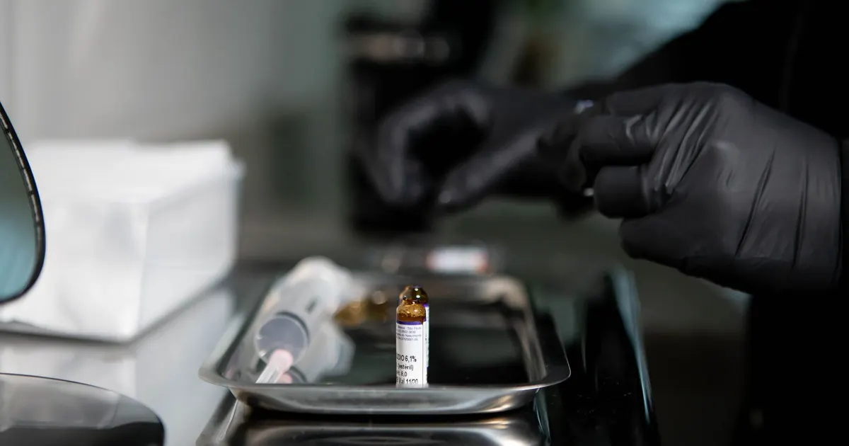 Manos con guantes preparando una jeringa junto a un vial sobre una bandeja metálica en un entorno clínico