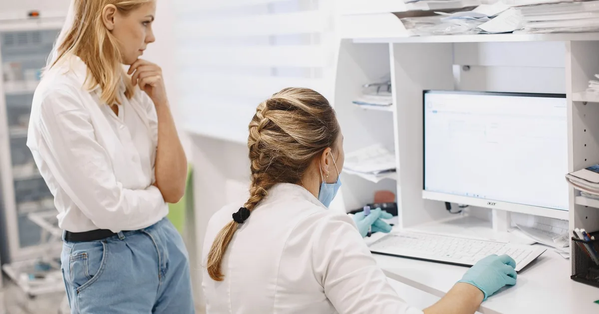 Dos trabajadoras de salud revisan datos en la pantalla de un computador en una clínica