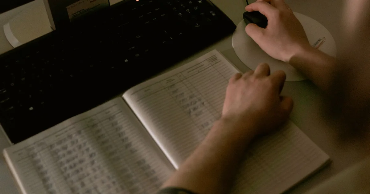 Trabajador de salud revisando datos médicos en una computadora junto a un cuaderno con anotaciones en una clínica