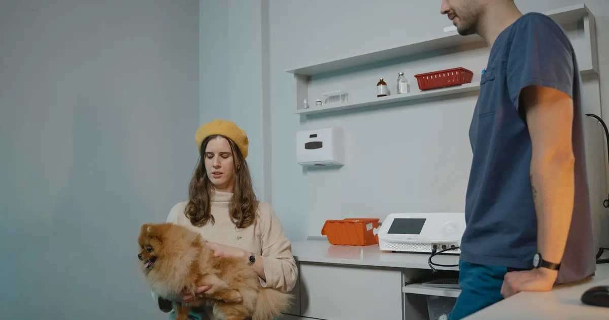 Una mujer con su perro Pomerania conversa con un veterinario durante una consulta en la clínica