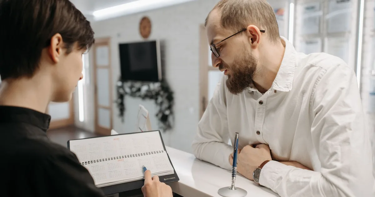 Una recepcionista conversa con un cliente sobre un turno en el mostrador de recepción de una clínica