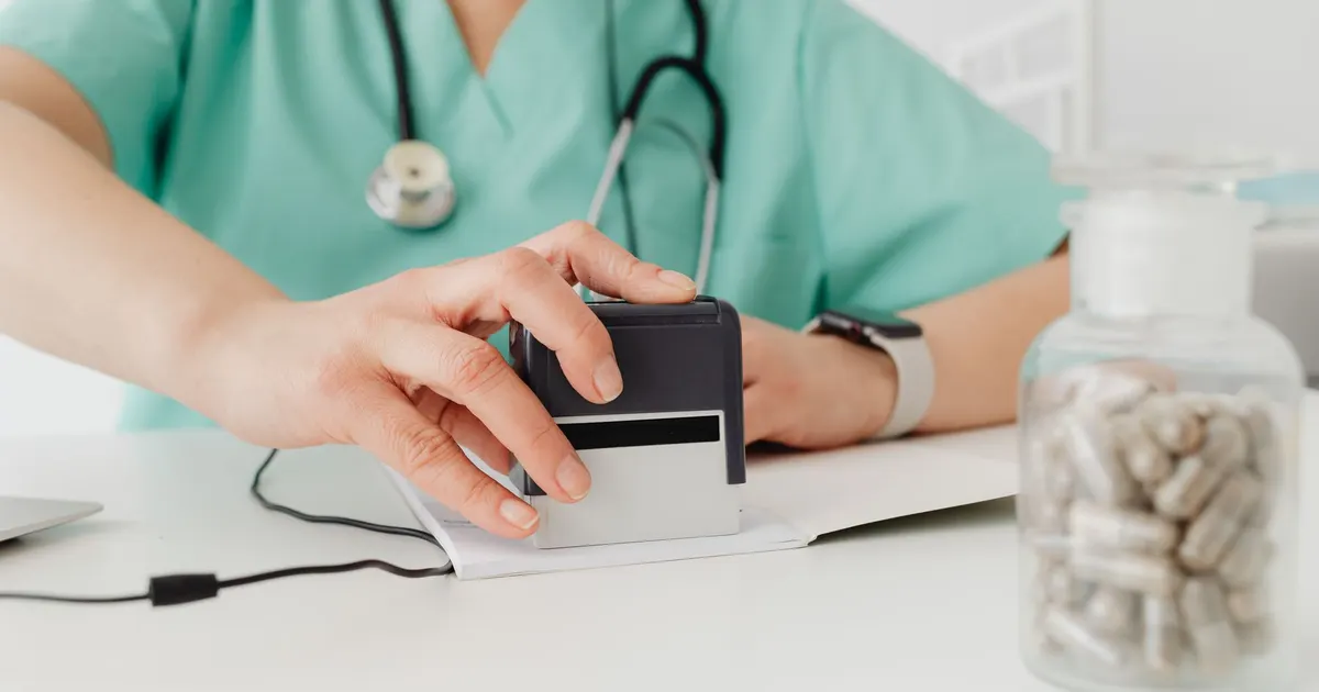 Primer plano de un doctor sellando una receta médica junto a un frasco de pastillas sobre el escritorio