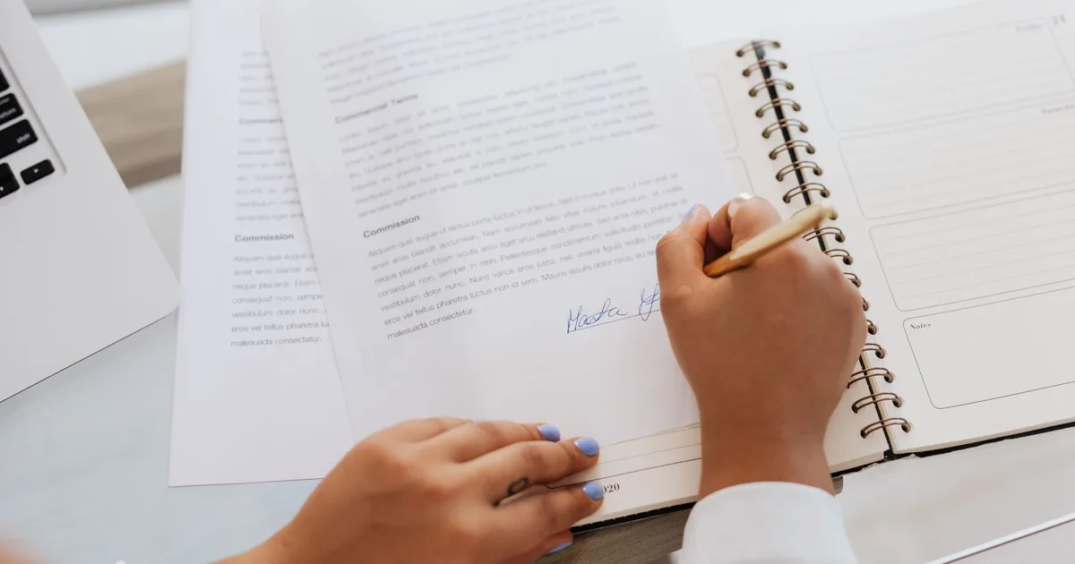 Primer plano de manos firmando un contrato sobre un escritorio con útiles de oficina