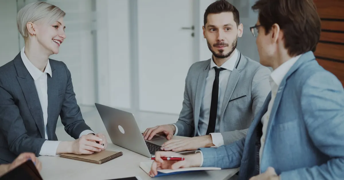 Profesionales reunidos en una mesa con laptops y cuadernos, conversando sobre estrategia y resultados
