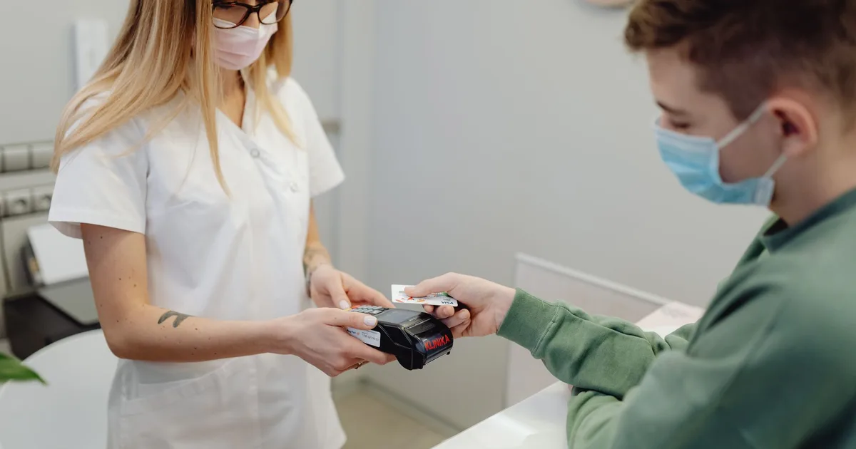 Profesional de salud procesa el pago con tarjeta de un paciente en la recepción de una clínica