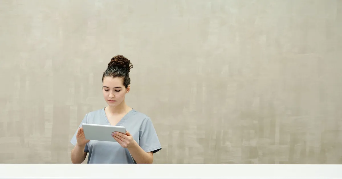 Mujer en uniforme usando una tablet en el mesón de recepción de una clínica