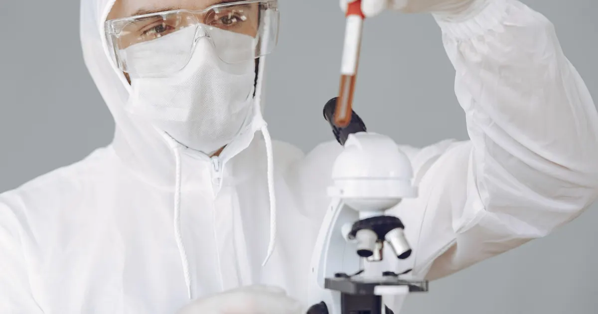 Persona con guantes y bata examina una muestra de sangre en un microscopio de laboratorio