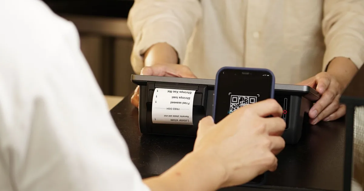 Dos personas realizan un pago sin contacto con código QR en el mostrador de un local