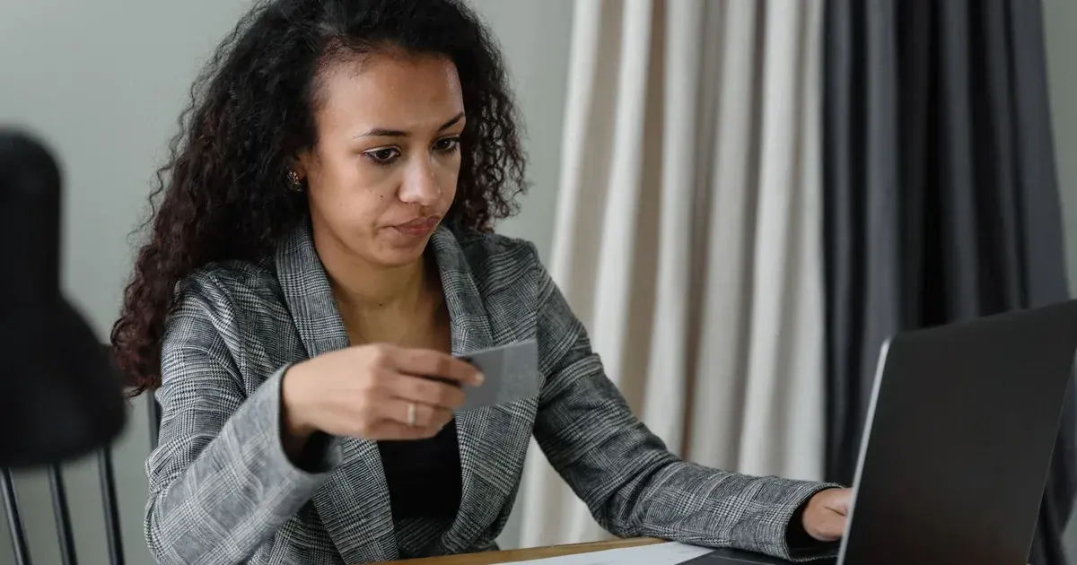 Mujer profesional revisa finanzas en su escritorio con tarjeta bancaria, laptop y efectivo